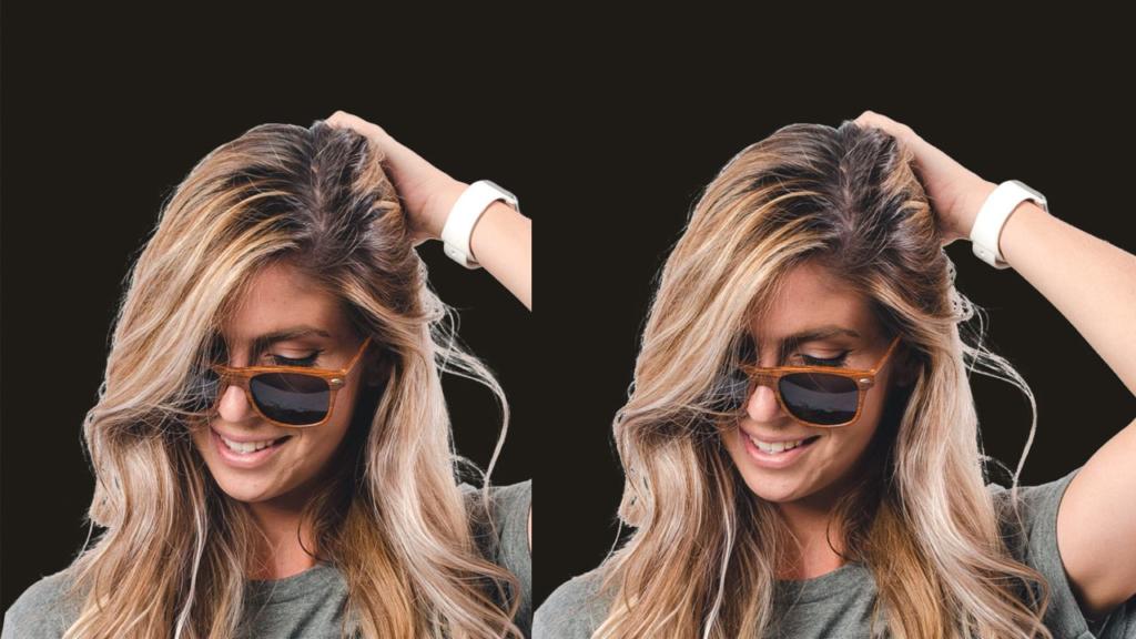 Une femme souriante aux longs cheveux blonds, portant des lunettes de soleil et une chemise grise, se tient les cheveux d'une main, comme pour détourner une chevelure. Elle porte une montre connectée blanche au poignet, sur fond noir uni.
