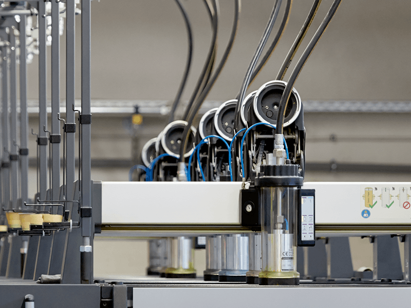 Des machines industrielles équipées de multiples bras robotisés et de tubes connectés, conçues pour les processus de fabrication, évoquent une scène de visite d'atelier de production. L'équipement est métallique, avec câblage et composants mécaniques visibles, et est situé à l'intérieur d'une usine.