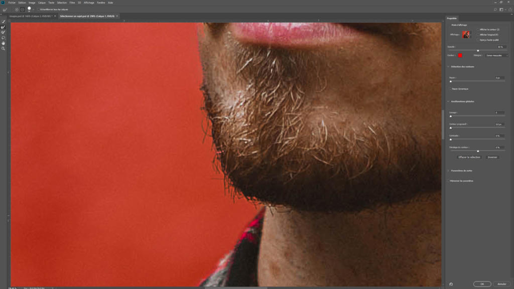 Gros plan sur le visage d'une personne portant barbe et moustache, accentué par des cheveux courts et ébouriffés. Le fond est rouge uni, rappelant l'utilisation de Photoshop pour créer cet effet en détourant une image ; une chemise en flanelle apparaît sur le côté. Les panneaux d'outils sont visibles à droite.