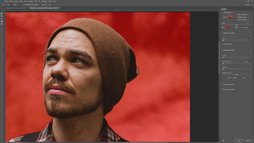 Un homme portant un bonnet marron, une barbe et une chemise à carreaux, regarde vers le haut. Sur un fond rouge vif, l'image semble avoir été retouchée avec les panneaux de réglage de Photoshop, comme pour détourner une image avec précision.