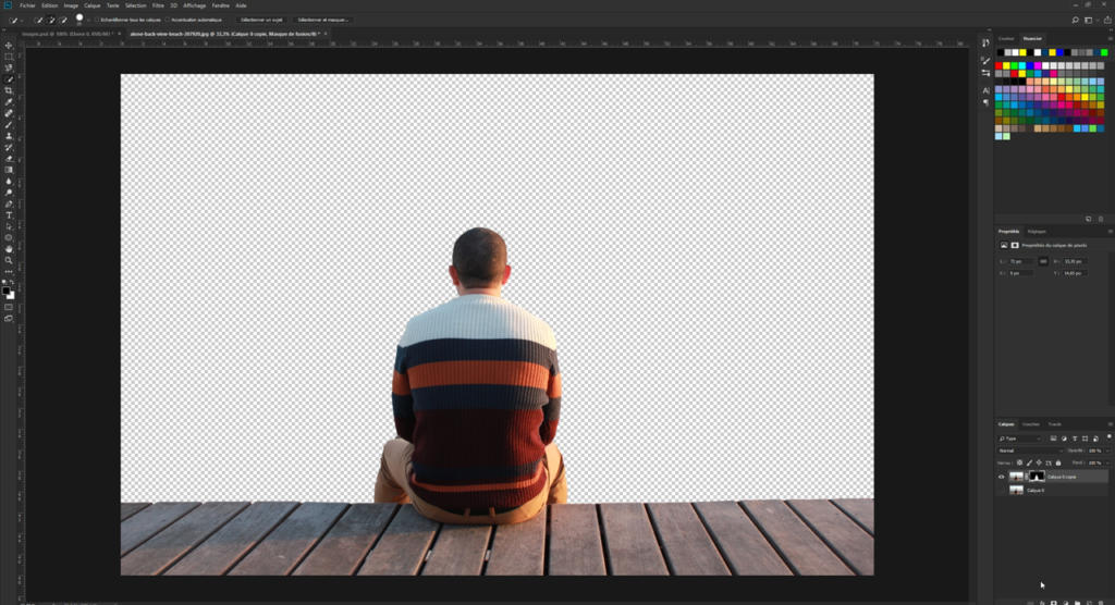 Une personne aux cheveux courts et portant un pull rayé est assise sur une terrasse en bois et réfléchit à la façon de retoucher une photo avec Photoshop. Elle se trouve face à un arrière-plan transparent, semblable à celui d'un logiciel de retouche photo.