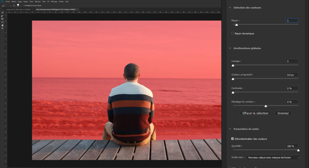 Une personne portant un pull rayé est assise sur une terrasse en bois face à un océan et un ciel teintés de rouge, apparemment engagée dans l'art de « flotter une photo avec Photoshop », avec des outils d'édition visibles sur la droite, suggérant qu'ils améliorent actuellement l'ambiance de l'image.