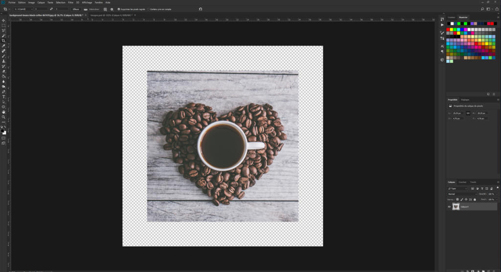 Une tasse de café noir est posée sur une surface en bois, entourée de grains de café disposés en cœur. L'image de cette scène enchanteresse s'affiche sur un écran d'ordinateur, un logiciel de retouche photo étant ouvert, prêt à rogner une image pour une composition parfaite.