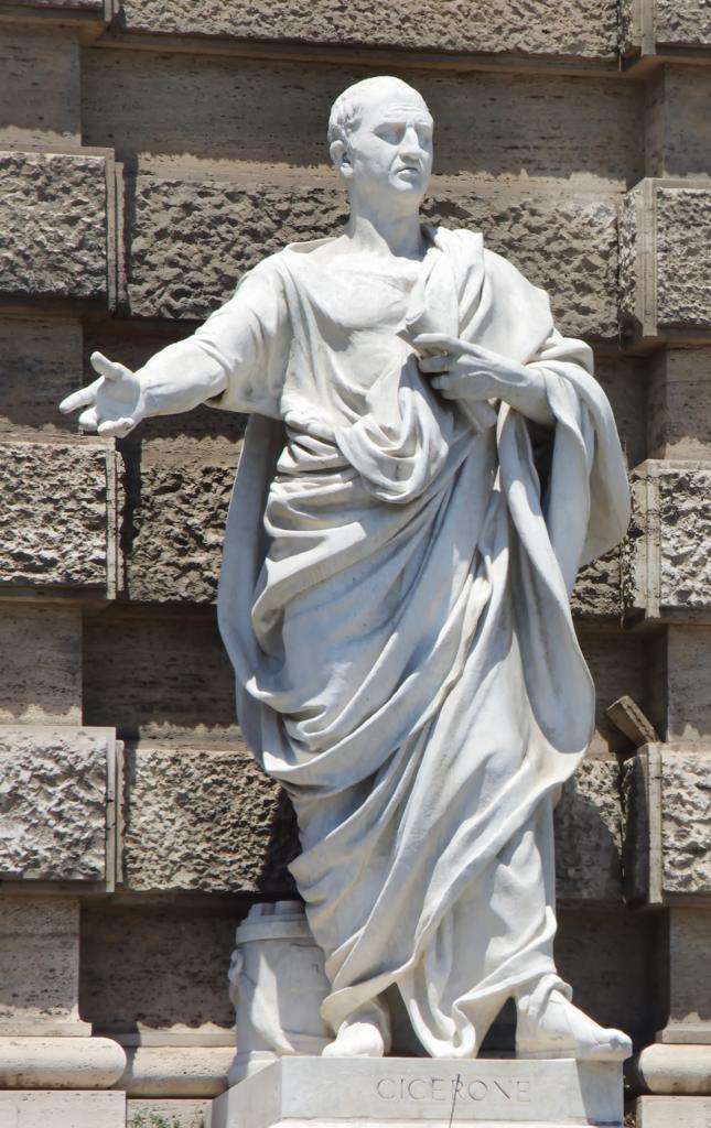 Statue en marbre représentant un homme en toge, un bras tendu vers l'extérieur. Un mur de briques est représenté à l'arrière-plan. Le piédestal porte l'inscription « CICERONE ».