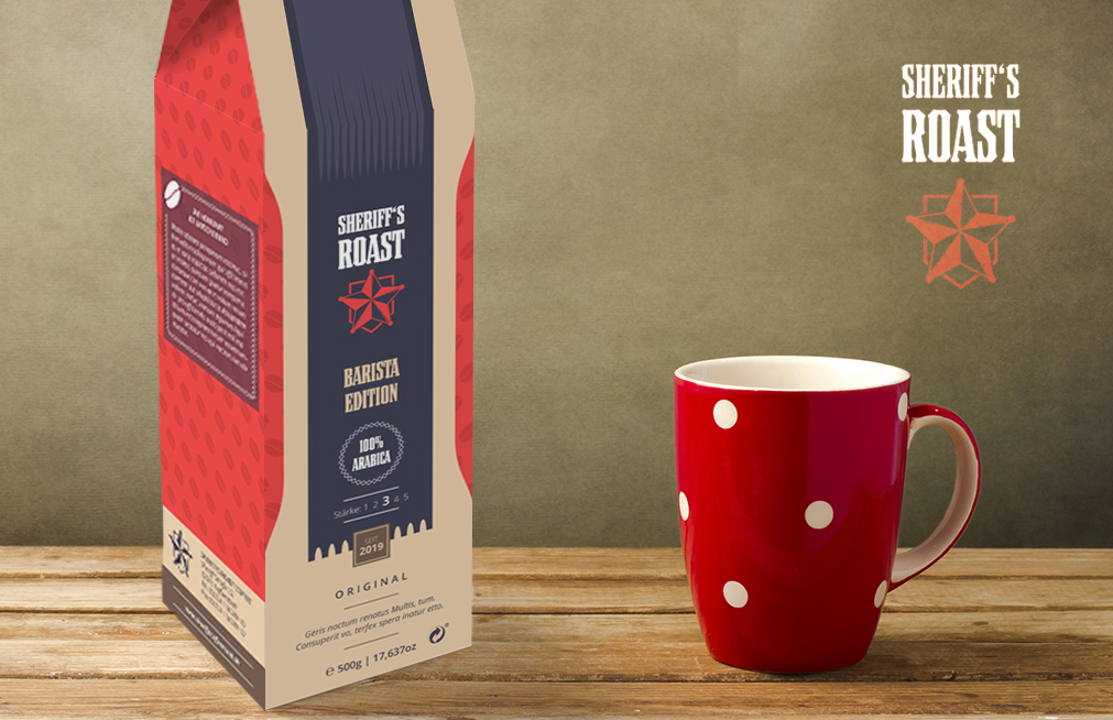 Un sac de café rouge et beige, étiqueté « Sheriff's Roast Barista Edition », au design élégant, est posé à côté d'une tasse rouge ornée de pois blancs sur une surface en bois. Le sac arbore un logo en forme d'étoile et des informations sur le mélange de café.