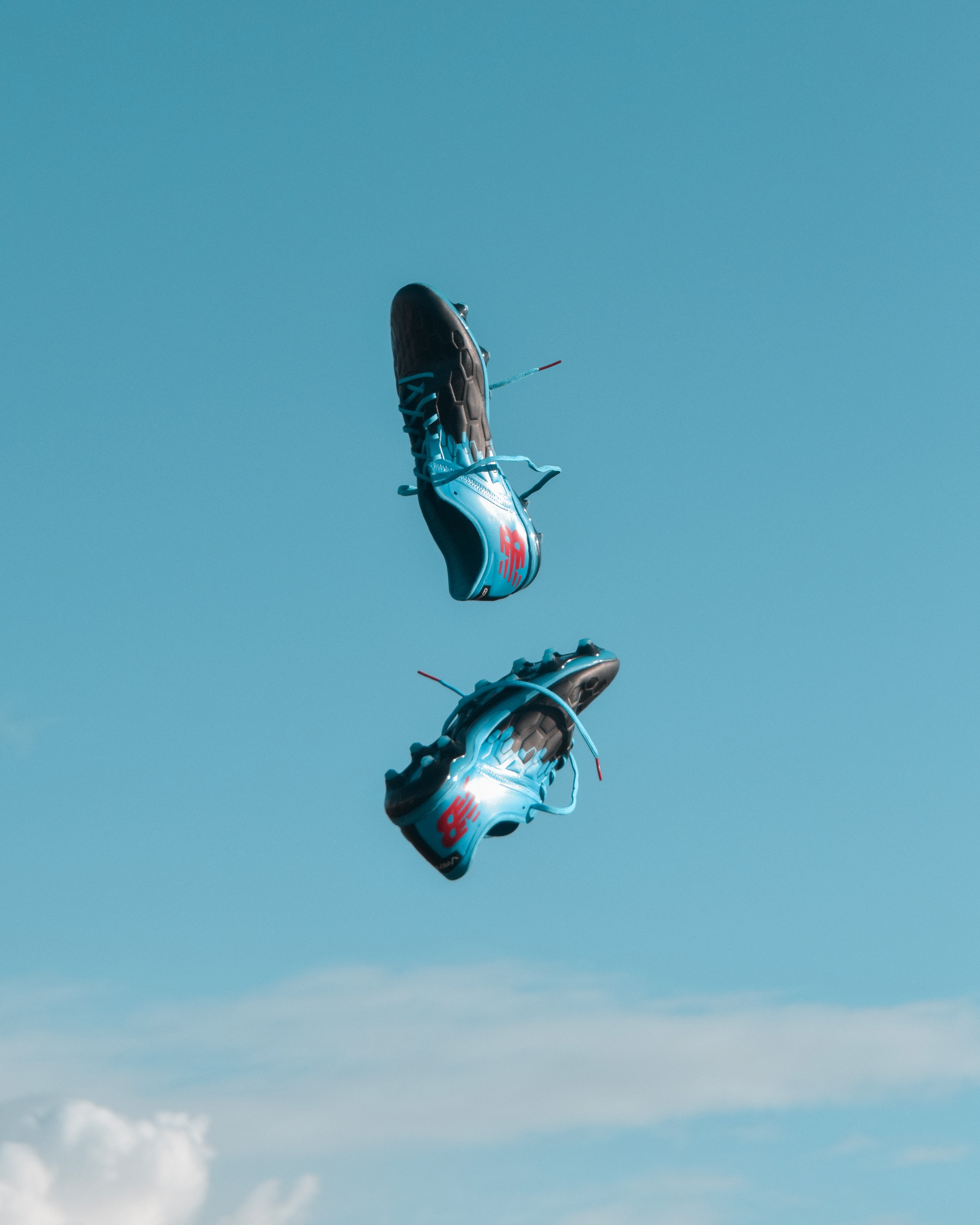 Deux chaussures de sport d'un bleu vif aux accents rouges flottent dans les airs sur un ciel bleu azur, rappelant l'effervescence du Spielplan de l'EM 2021. Légères, elles mettent en valeur le mouvement et la vitesse, tandis que des touches de nuages blancs ajoutent une touche onirique.