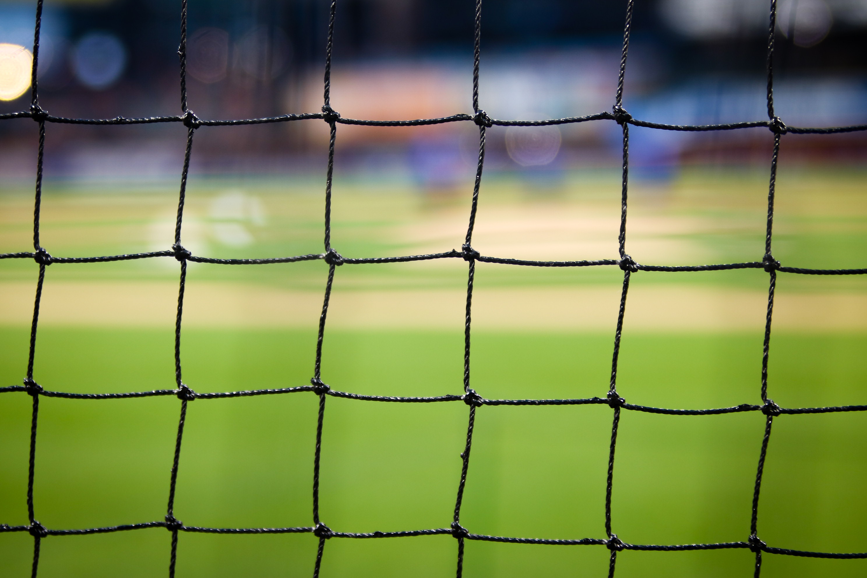 Gros plan d'un filet de sport noir sur fond flou, mettant en valeur un terrain gazonné rappelant un stade de l'EM 2021. Le filet est net, le terrain vert formant un arrière-plan doux et contrasté.