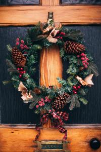 Une couronne de Noël festive, ornée de pommes de pin, de baies rouges et de décorations en toile de jute, est suspendue à une porte en bois. En dessous, une fente à lettres intitulée « Lettres » est ornée d'un ruban écossais.
