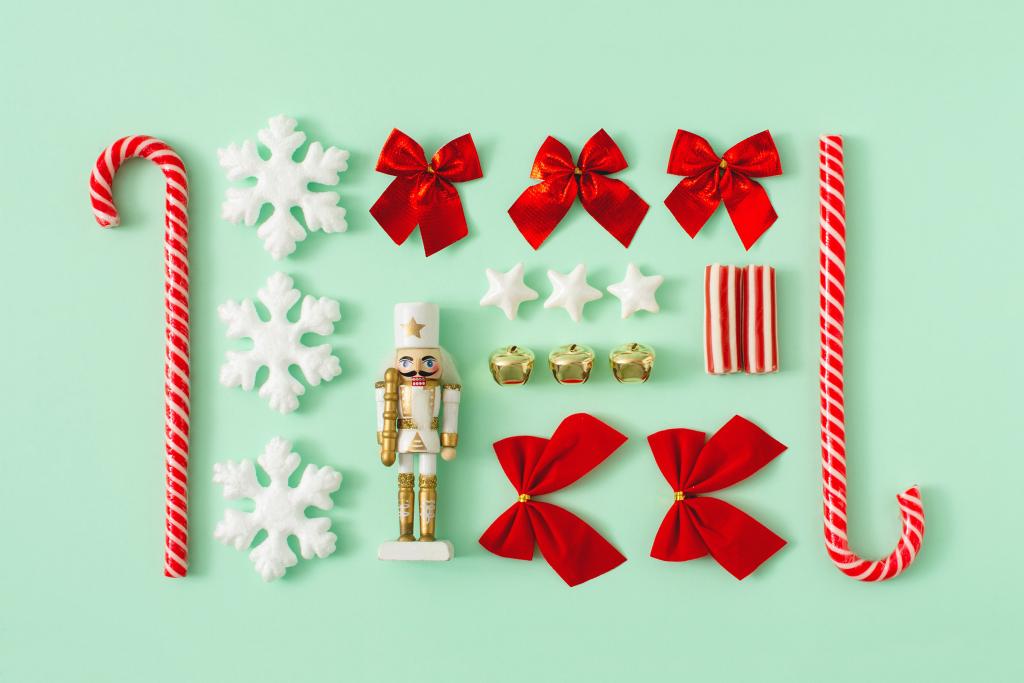 Un ensemble d'objets sur le thème de Noël sur fond vert menthe. Comprend des cannes de bonbon, des flocons de neige, un casse-noisette, des clochettes dorées, des nœuds rouges, des étoiles blanches et un bonbon rayé, le tout disposé symétriquement.