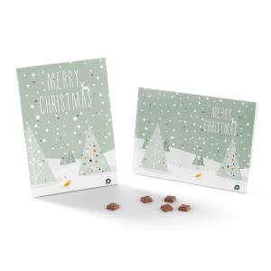 Deux cartes de Noël vertes avec le texte « Joyeux Noël » et des sapins triangulaires sous la neige. Les cartes sont partiellement dépliées, avec plusieurs petites friandises brunes posées devant elles sur une surface blanche.